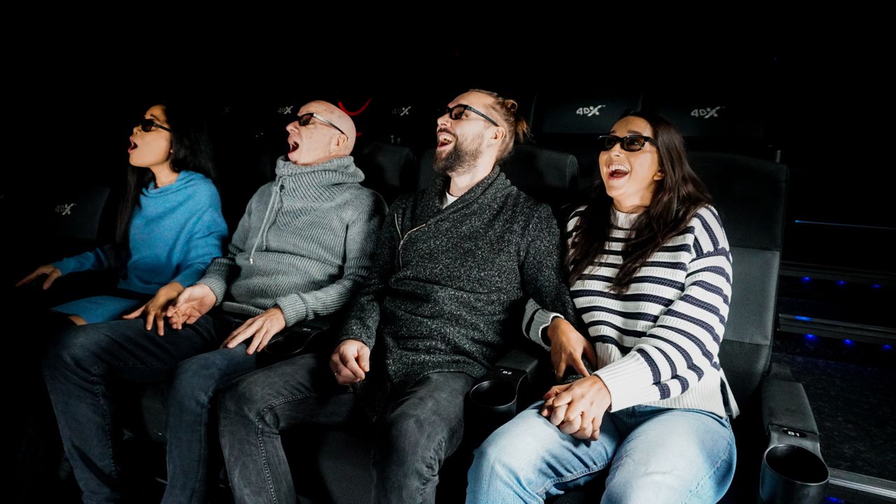 Vier Personen sitzen in Kinosesseln nebeneinander und blicken staunend auf die Leinwand