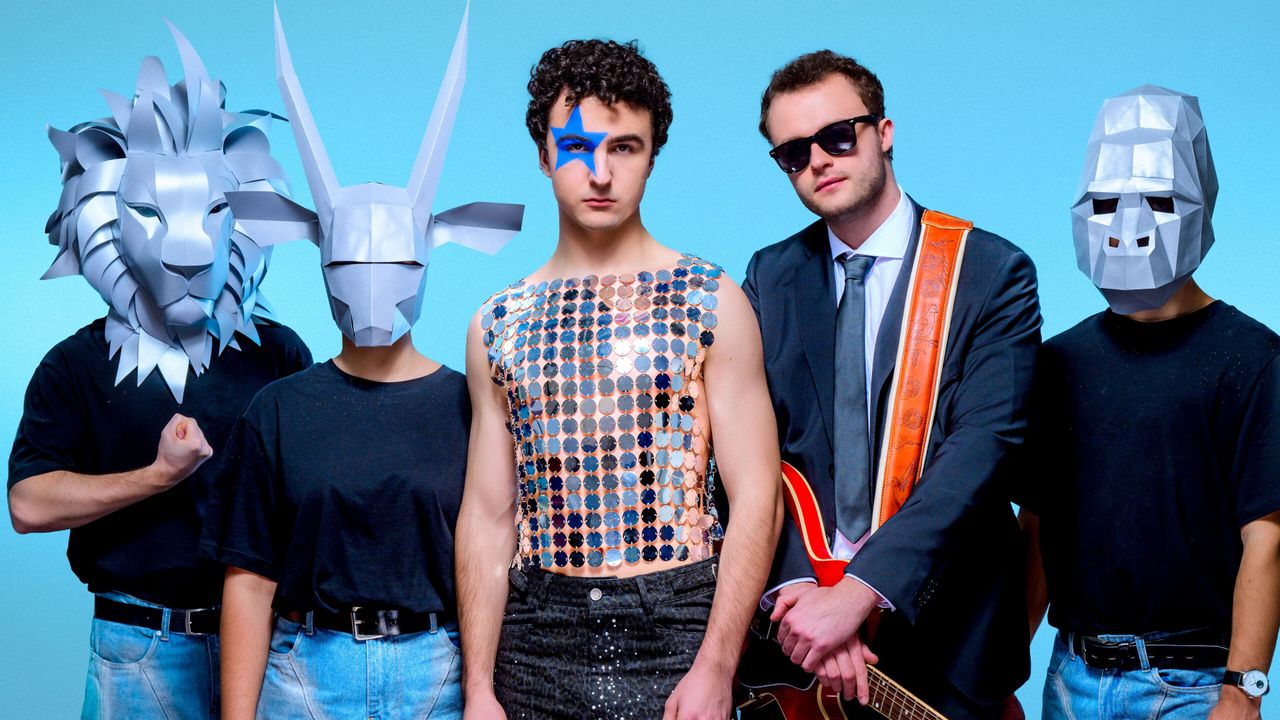 Cosmó steht mit seiner Band vor einer blauen Wand