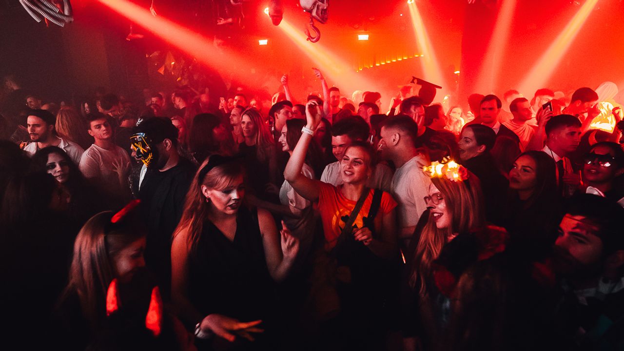 Verkleidete Partygäste tanzen bei roter Lasershow