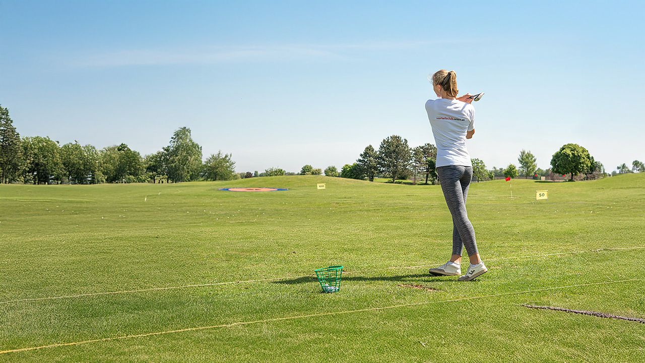 Eine Frau, die einen am Golfplatz steht und einen Golfschläger schwingt