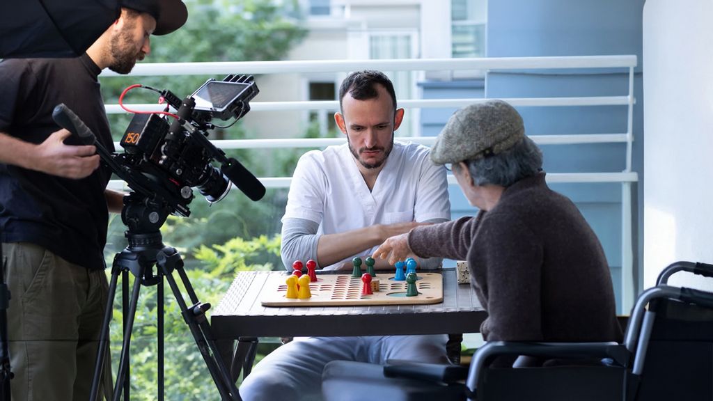 Ein Mann, der an einem Tisch sitz und ein Brettspiel spielt und dabei gefilmt wird