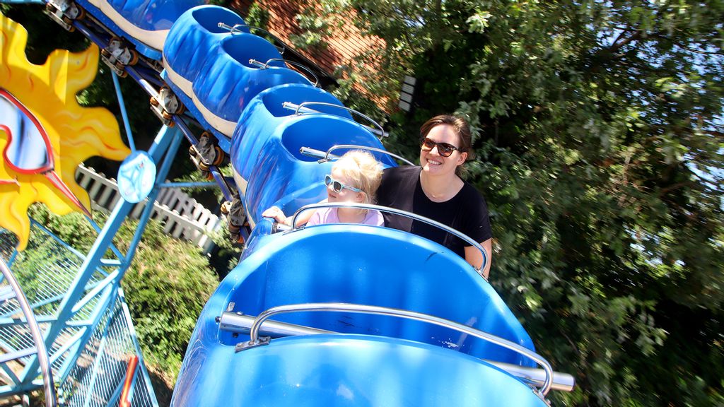 Eine Frau mit einem Kind sitzen in einer blauen Achterbahn für Kinder
