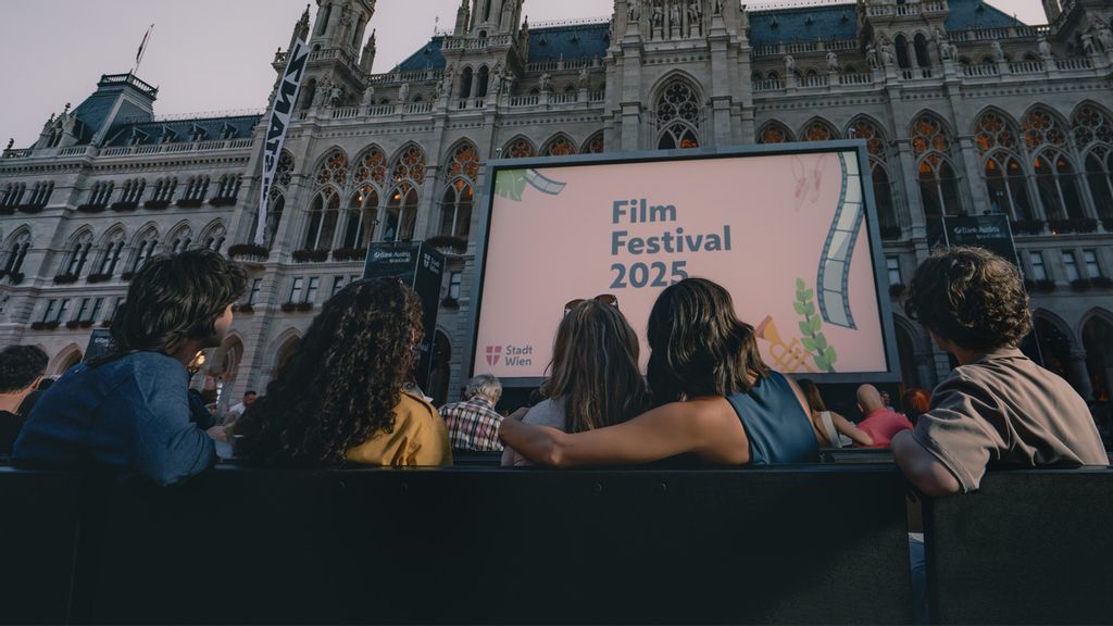 © Flo Mitteregger Fünf Personen von hinten, die auf eine Leinwand schauen, die vor dem Wiener Rathaus steht.