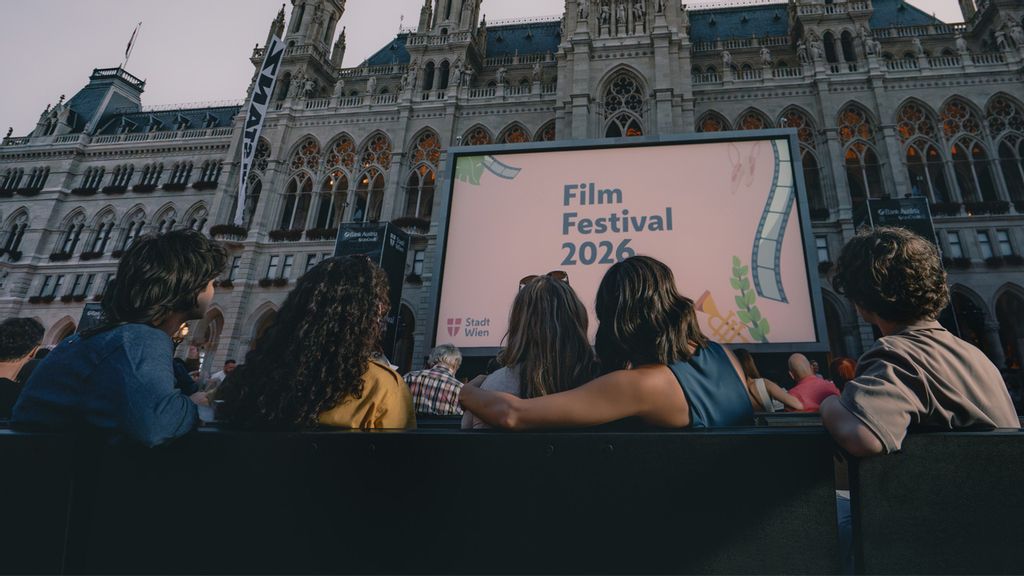 Eine Gruppe von Personen sitzen und blicken auf eine große Leinwand vor dem Wiener Rathaus