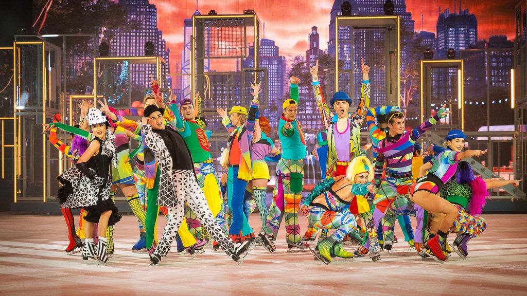 Eine Gruppe von Menschen in bunter Kleidung und Eislaufschuhen tanzen auf einer Eisfläche