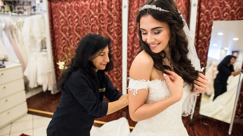 Eine Frau in einem Brautkleid, die von einer Verkäuferin betreut wird