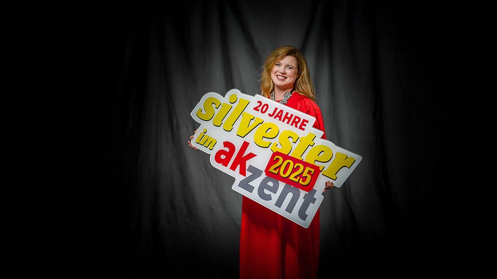 Eine Frau in rotem Kleid hält ein Schild in der Hand worauf "20 Jahre Silvester im Akzent" steht