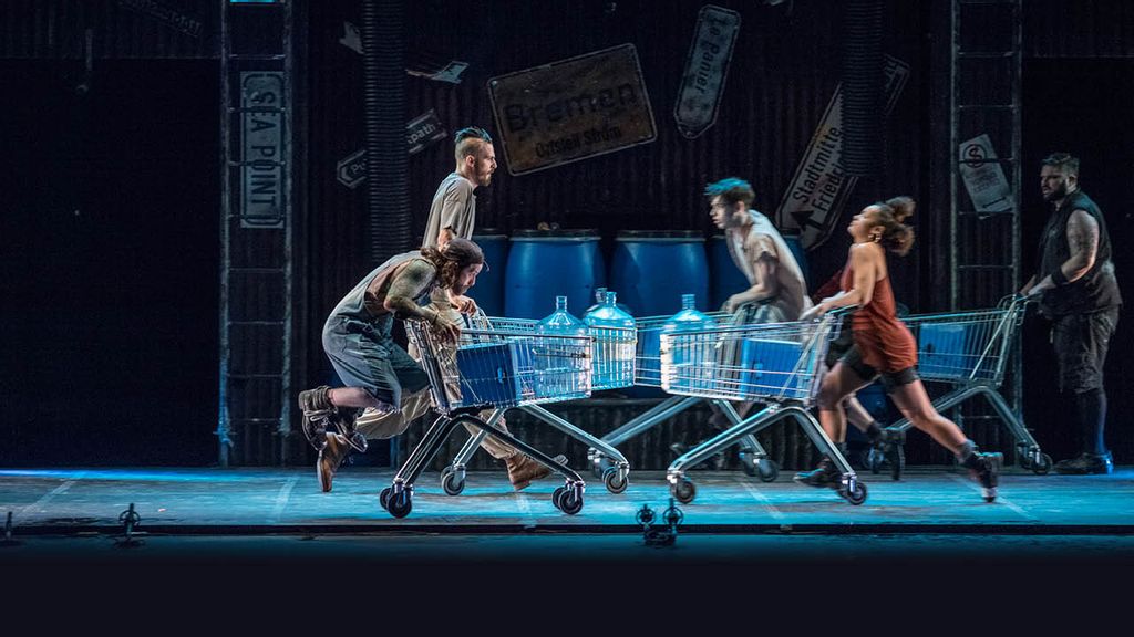 5 Menschen auf einer Bühne, die Einkaufswägen schieben und tanzen