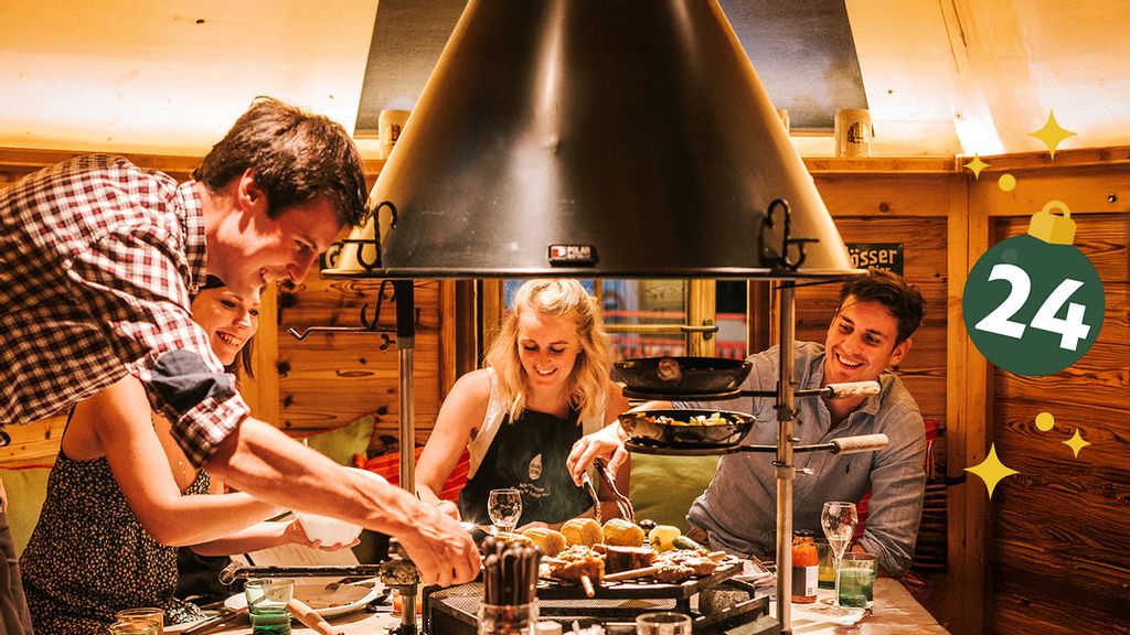 Sechs Personen sitzen in einer gemütlichen Holzhütte mit einem Griller in der Mitte