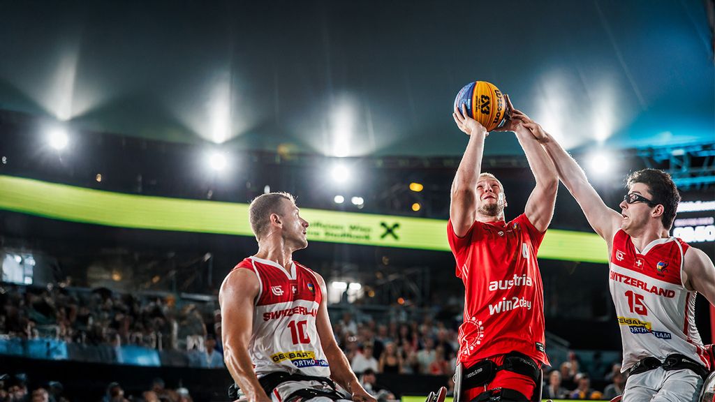 Drei Basketballspieler bei einem Turnier, einer wirft einen Basketball