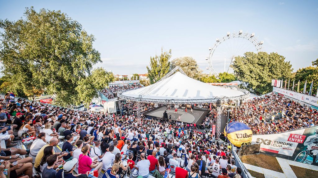 Eine überdachte Bühne mit vielen Zuschauer*innen rundherum und das Wiener Riesenrad im Hintergrund