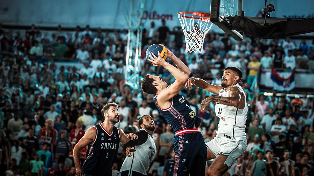 Vier Basketball Spieler in Trikots und einer mit einem Ball in der Hand, der auf den Korb zielt