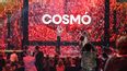 Ein Mann auf einer Bühne die rot beleuchtet ist und wo im Hintergrund COSMÓ steht