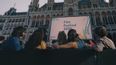 Eine Gruppe von Personen sitzen und blicken auf eine große Leinwand vor dem Wiener Rathaus